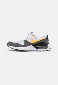Sneaker bianca con inserti in suede grigio e suola in gomma nera, caratterizzata da uno swoosh giallo di Nike, tomaia in mesh e un'unità Air visibile nel tallone.