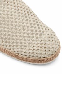 Beżowe buty z tkaniny o plecionym wzorze z otwartym siateczkowym designem i zaokrąglonym noskiem. Korkowa podeszwa z delikatnie teksturowanym wykończeniem. Geometriczny wzór na górze.