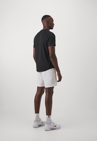 Camiseta negra de manga corta, pantalones cortos blancos, zapatillas deportivas. Diseño simple, colores sólidos, estilo ajustado, tejido texturizado. Modelo posicionado de lado.
