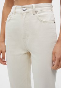 Vaqueros de mezclilla beige con cintura alta, bolsillos frontales y cierre con botón plateado. La tela tiene una textura suave y un sutil ribete diagonal.