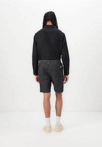 Chemise noire à manches longues, short en denim gris, et baskets claires. Le short est doté d'une taille élastique et de poches arrière. Design minimaliste.