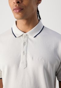 Hellgraues Poloshirt aus strukturiertem Stoff, mit einem Kragen in Marineblau und drei Knöpfen an der Knopfleiste, dezent gebrandet.