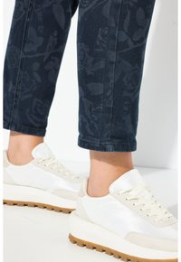 Bílé a béžové tenisky s texturovaným textilním svrškem, kulatou špičkou a gumovou podrážkou. Tmavé džíny s květinovým vzorem, zkrácené na kotníky.