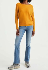 Yellow ribbed sweater with a wide neckline, paired with light blue flared jeans and gray sneakers with accents.