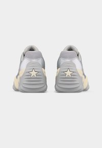 Ζευγάρι γκρι και μπεζ αθλητικών παπουτσιών, εμφανιζόμενα από πίσω, με αστέρι ως λεπτομέρεια στη φτέρνα κάθε παπουτσιού, σε λευκό απλό φόντο.