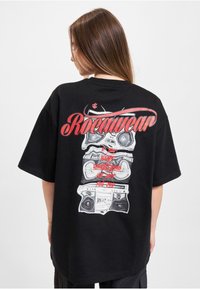 Black oversized t-shirt featuring a graphic print of stacked boomboxes in white and red with "Rocawear" text above in bold red lettering.