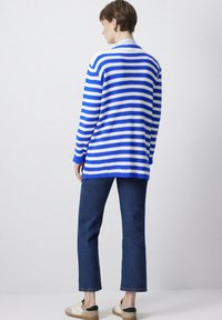 Cardigan tricoté rayé bleu et blanc avec une coupe décontractée, associé à un jeans droit bleu marine et des baskets beige. Look simple et décontracté.