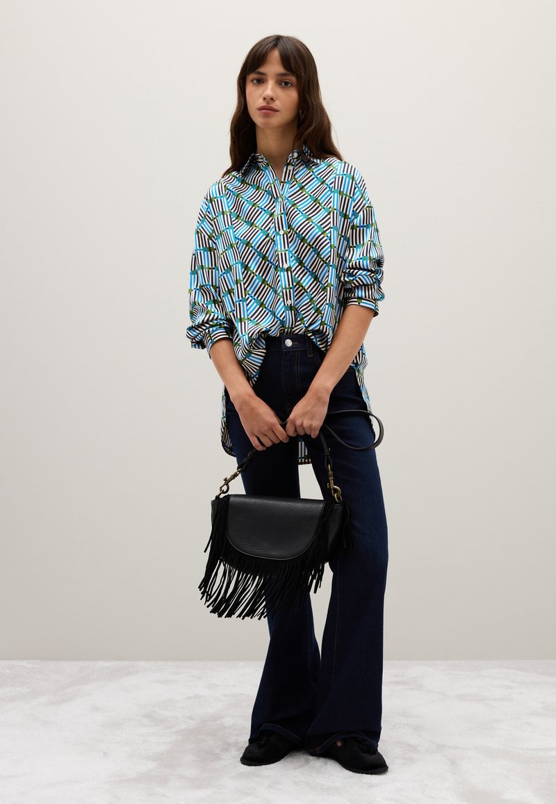 Chemise à motifs en bleu, vert et noir ; pantalon en denim foncé évasé ; sac à franges noir avec quincaillerie dorée ; arrière-plan doux et texturé.