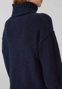 Navy Strick-Turtleneck-Pullover mit geripptem Kragen, strukturiertem Stoff, überschnittenen Schultern und weiten Ärmeln. Taillierte Passform mit geripptem Saum.