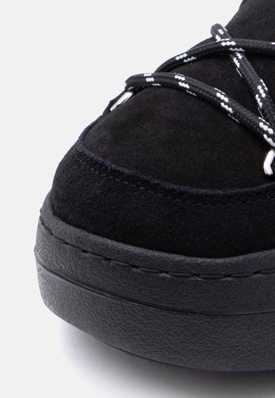 Μαύρο σουέντ αθλητικό παπούτσι με ανάγλυφη μαύρη καουτσούκ σόλα. Διαθέτει σταυρωτά μαύρα και λευκά κορδόνια και λεπτομέρεια ομαλής ραφής.