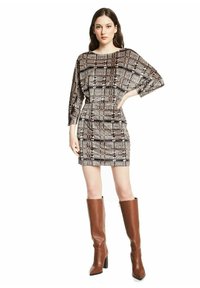 Korte mouwen, getailleerde jurk in een zwart, wit en bruin herringbone patroon. Voorzien van een ronde halslijn en gecombineerd met bruin kniehoge laarzen.