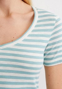 Camiseta de rayas azul claro y blanca con textura acanalada, escote en forma de V y mangas cortas. Presenta una vista en primer plano de la parte superior de la tela.