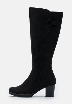 Botte noire en suède montant jusqu'au genou, avec talon bloc, bout arrondi, coutures décoratives et bride latérale ornée d'un anneau en métal.