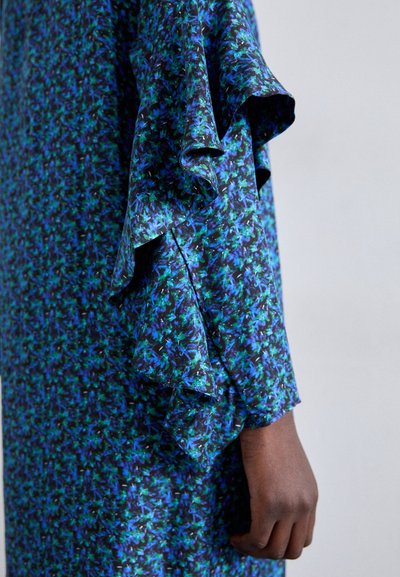 Bla dresses mit Rüschensäumen, aus strukturiertem Stoff gefertigt und mit einem dunklen Hintergrund, der mit komplexen grünen und blauen Mustern verziert ist.