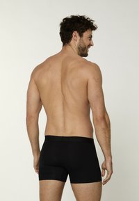 Boxer neri con una cintura morbida, tessuto liscio e design aderente, mostrati da un'angolazione laterale su uno sfondo neutro.