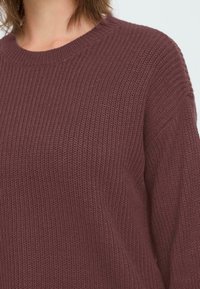 Burgundy neulepaita, jossa on ribbikuvio, ympyräkaulus ja pitkät hihat. Kangas näyttää pehmeältä ja paksulta.