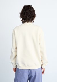 Sweat-shirt couleur crème avec une coupe décontractée, des poignets et un ourlet côtelés, présentant un design simple et une texture douce. Vue arrière affichée.