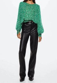 Blouse à motifs verts avec des manches bouffantes, associée à un pantalon en cuir noir taille haute, avec des jambes droites et des passants pour ceinture.