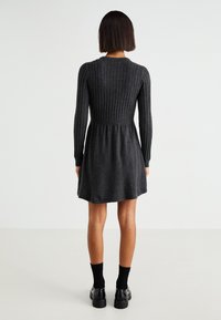 Robe tricotée côtelée gris foncé avec des manches longues, un bustier ajusté et une jupe évasée. Texture lisse, longueur genoux, associée à des chaussettes et des chaussures noires.