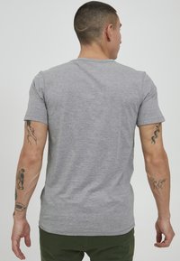 Gray short-sleeve t-shirt made of soft cotton fabric, featuring a classic crew neckline and a fitted shape. Notable tattoos visible on arms.