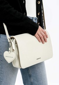 Weiße Leder-Crossbody-Tasche mit strukturierter Oberfläche, ausgestattet mit einem Klappenverschluss und einem herzförmigen Anhänger mit der Aufschrift "EMILY & NOAH."