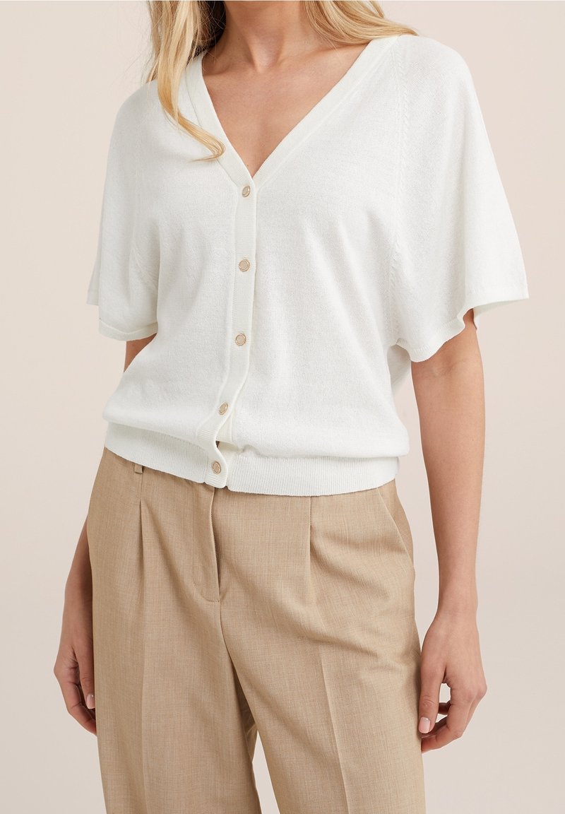 Cardigan bianco con maniche corte e scollo a V, dotato di chiusura con bottoni. Realizzato in tessuto morbido, presenta una vita fitted e una trama delicata.