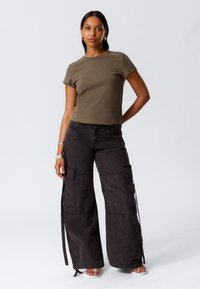 Tricou ajustat de culoare verde măslin, cu mâneci scurte, asortat cu pantaloni cargo negri, lejeri, care au multiple buzunare și fermoare pe lateral.