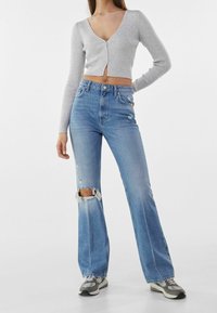 Grå rippad kortstickad tröja med V-hals, kombinerad med ljusblå höga flare-jeans med knäskärningar och fransade kanter.