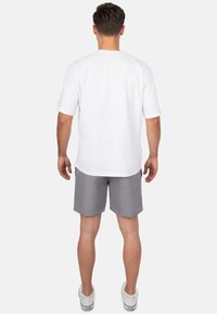 T-shirt blanche à manches courtes associée à un short gris. Le t-shirt a un col rond et le short est doté d'une poche et d'un design simple.