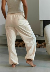 Pantalons élastiques beige clair à taille avec poches latérales et chevilles ajustées, fabriqués à partir d'un tissu doux et texturé. Convient pour une tenue décontractée.
