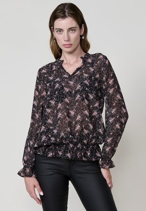 Blusa negra con flores, de mangas largas, puños con volantes, escote en V y dobladillo fruncido; presenta patrones florales en rosa, blanco y verde sobre una tela transparente.