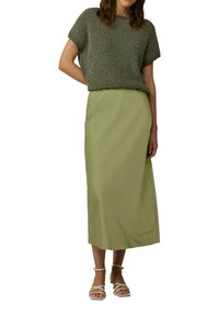 Grünes Strickoberteil mit kurzen Ärmeln, kombiniert mit einem langen, hellgrünen Satinrock. Das Model trägt weiße Sandalen mit Riemchen.