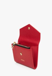 Czerwony skórzany portfel o teksturowanej powierzchni, ze złotym zamknięciem na zamek błyskawiczny i zapięciem na zatrzask. Posiada sześciokątną klapkę. Widoczne logo marki.
