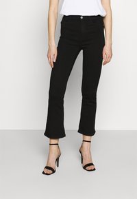 Jeans negros de campana con una textura suave y un diseño ajustado, que cuentan con un cierre de botón y cremallera, combinados con tacones negros de tiras.
