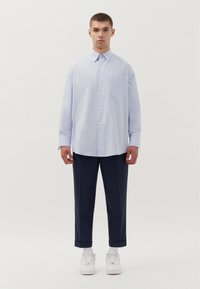 Camicia button-up a righe azzurro chiaro con maniche lunghe, una tasca, abbinata a pantaloni blu navy e sneakers bianche. Design semplice, vestibilità comoda.