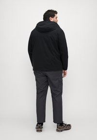 Black hooded jacket with a smooth texture, paired with gray cargo pants featuring side pockets, and black sneakers with brown accents.