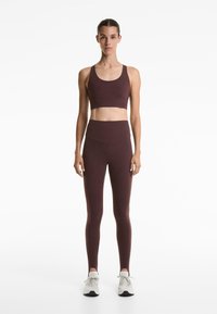 Maroon sports bra with a wide underband paired with high-waisted maroon leggings, featuring a smooth texture and fitted design.