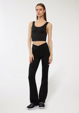 Top corto nero e pantaloni svasati realizzati in tessuto liscio e elasticizzato. I pantaloni presentano una vita incrociata e sono abbinati a sneaker nere.