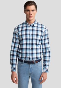 Heren overhemden met knopen in een blauw, wit en marineblauw geruit patroon. Gemaakt van katoen, met lange mouwen en twee borstzakken. Draagt bij lichte spijkerbroeken.