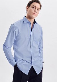 Hellblaues Langarmhemd mit Knopfkragen, Brusttasche und kontrastierenden dunklen Kragenakzenten, gefertigt aus glattem Stoff.