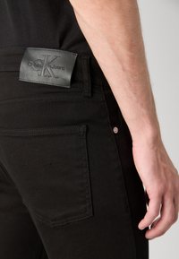 Černé džíny z denimu se štepováním, viditelnou zadní kapsou a černým koženým štítkem s logem 'Calvin Klein Jeans'.