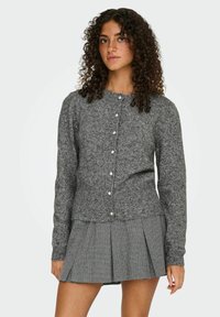Cardigan tricoté gris avec encolure arrondie et fermeture à boutons, présentant un tissu texturé et des poignets côtelés, associé à une jupe plissée grise.