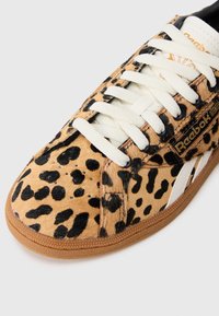 Reebok tenisice s leopard uzorkom, s teksturiranim gornjim dijelom nalik krznu, bijelim vezicama i smešnim gumenim đonom. Sadrže detalj s logotipom sa strane.