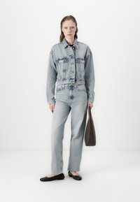 Denim jakna i traperice svijetloplave boje, s krojenjem na visokom struku, prednjim džepovima i zatvaranjem na patentni zatvarač. Crne balerinke i smeđa torba upotpunjuju izgled.