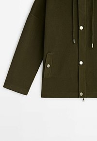 Veste longue à manches longues vert foncé avec boutons-pression à l'avant, fermeture éclair, deux poches latérales à boutons-pression, et cordons de capuche réglables.