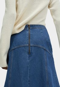 Denimkjol med bakdragkedja, hög midja och utsvängd silhuett med kontrasterande sömmar på ett medelblått tyg.