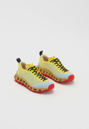 Žluté a modré síťované tenisky s hnědým mezipodešvem a červenou podrážkou. Mají černé tkaničky a zadní poutko. Texturovaný povrch.