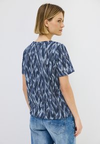 Kortärmad t-shirt i mörkblått med ett mönster av ljusblå penseldrag. Mjukt tyg, rund halsringning och avslappnad passform.