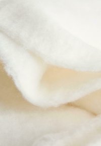 Tissu blanc doux avec une texture pelucheuse, présentant une forme fluide et lisse, ainsi que des couches créant de la profondeur et de la dimension.
