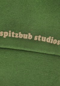 Grüner Strickstoff mit einem strukturierten Muster. Die Wörter "spitzbub studios" sind in hellbeige über die Oberfläche gedruckt.